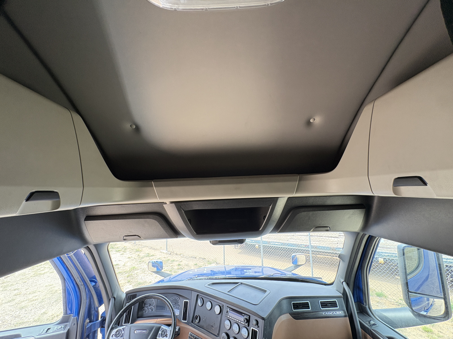 Cab interior of a Freightliner Cascadia 126 truck showing dashboard gauges and steering wheel, with blue exterior visible through windows.
