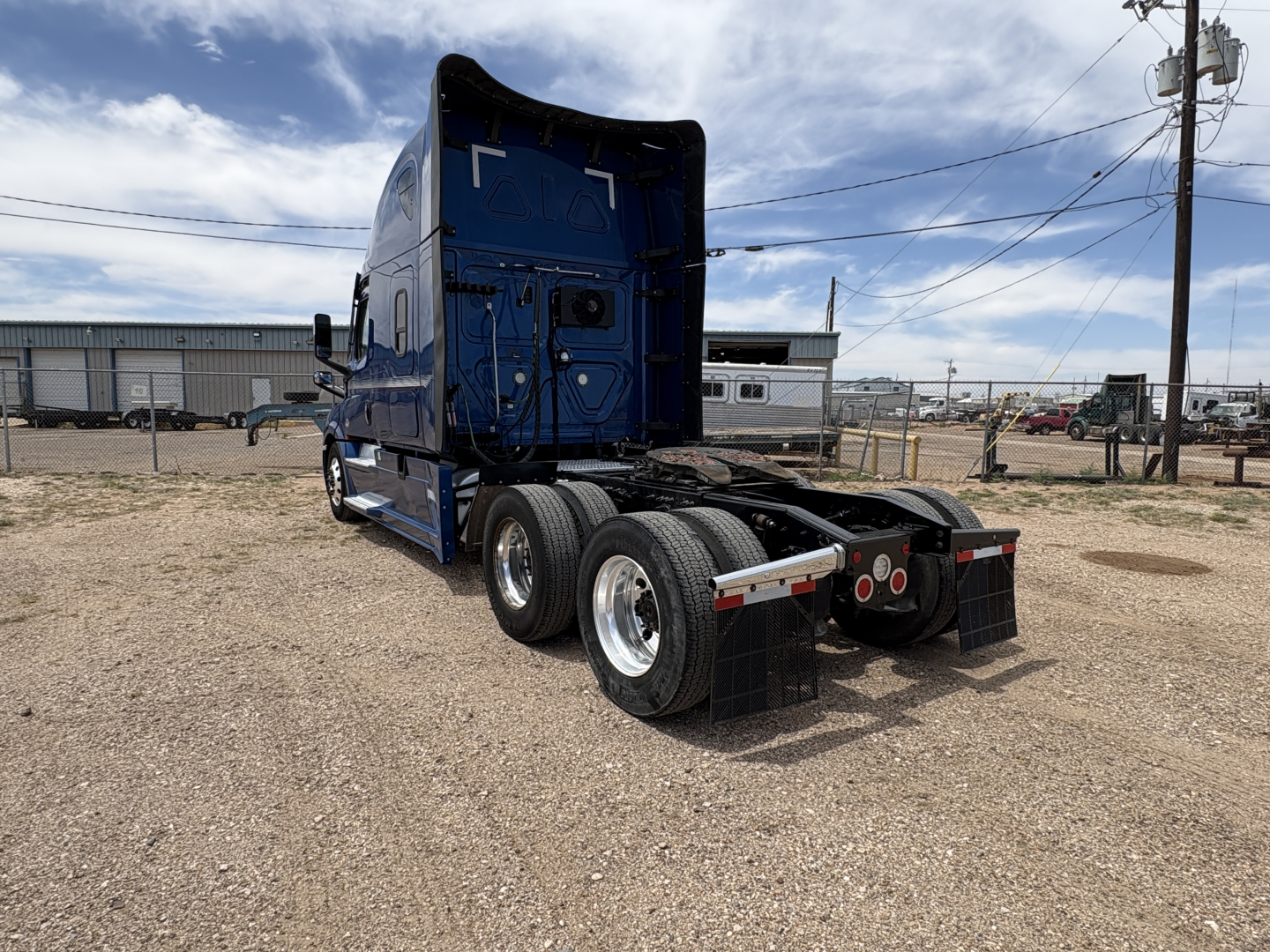 Rear view of a blue Freightliner Cascadia 126 tractor on a gravel lot, showing the sleeper cab and fifth-wheel area with dual rear axles and mud flaps.