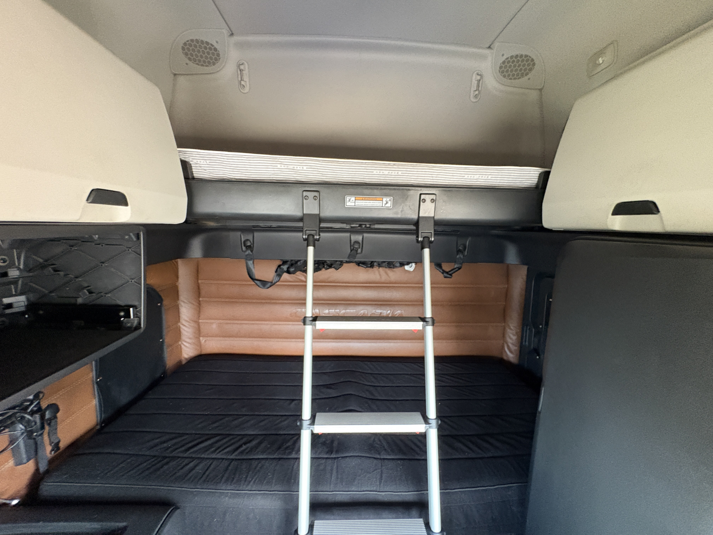 Semi truck sleeper cab interior showing bed area with ladder, storage cabinets, and bunk space inside a Freightliner Cascadia 126.