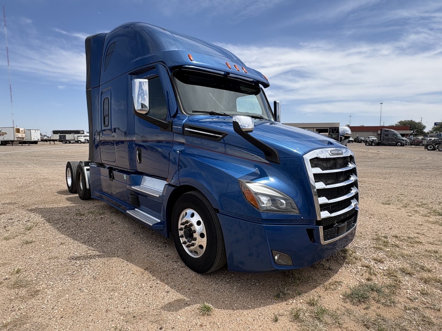 Truck cab interior and exterior of a blue 2022 Freightliner Cascadia 126 conventional sleeper tractor, front-left view, with chrome grille, dual rear axles, and daylight surroundings.