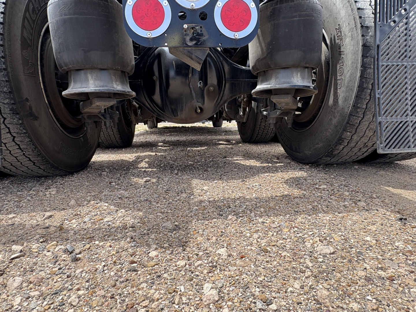 Underside of a Freightliner Cascadia 126 tractor showing rear suspension, driveshaft, and dual rear axles with tires; visible hub assemblies and mud guards.