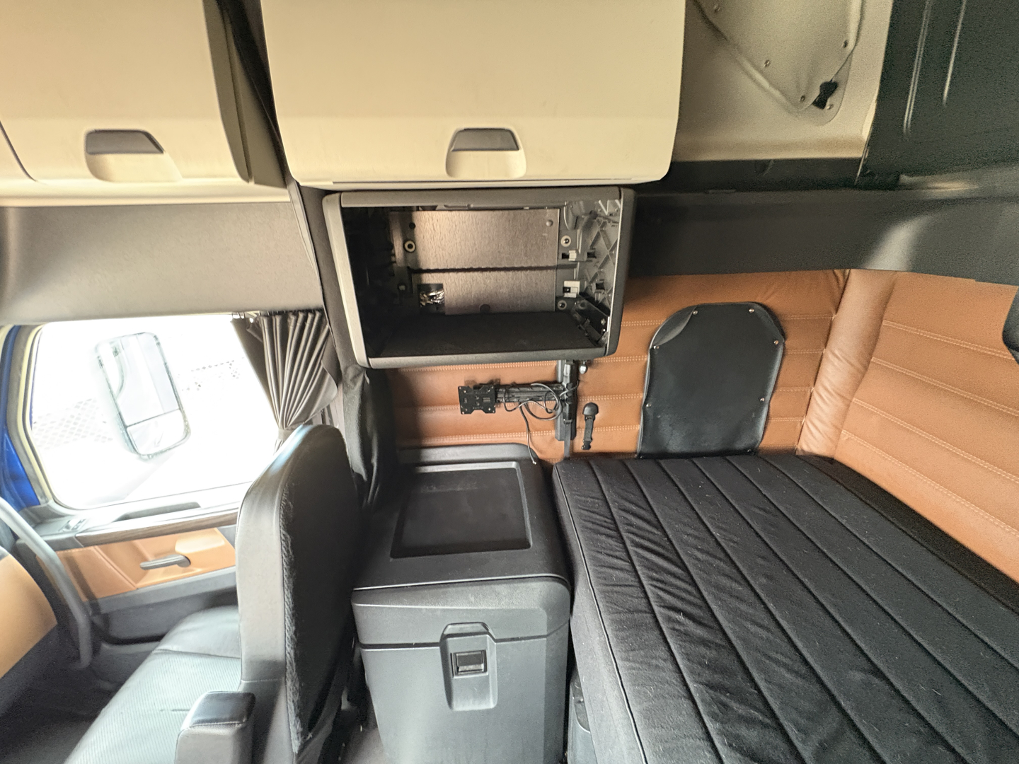 Freightliner Cascadia 126 cab interior showing overhead cabinet open, storage box, and back sleeper area with bench seating and paneling.