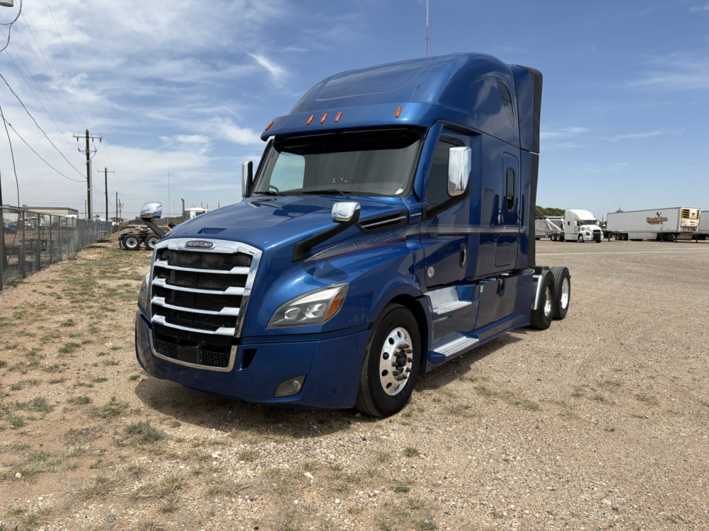 Truck image: blue 2022 Freightliner Cascadia 126 sleeper cab, front-left view showing grille, headlights, and side profile on a gravel lot.