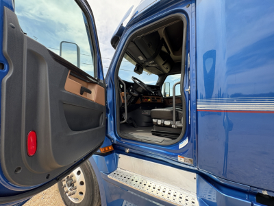 Truck cab interior and open door of a blue 2022 Freightliner Cascadia 126 showing the driver's seat, dashboard, and entry step.