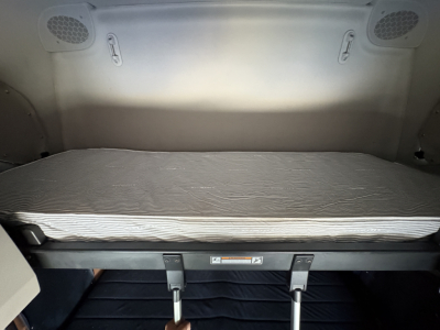 Truck cab interior showing a raised sleeper bed platform with a thin mattress, overhead ceiling, and side panels.