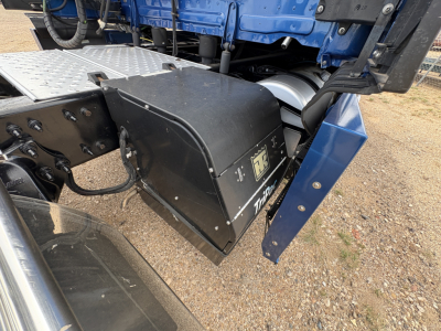 Truck component bay showing undercarriage area with black storage box and blue frame, Freightliner CASCADIA 126 cab seen, wiring and metal steps nearby.