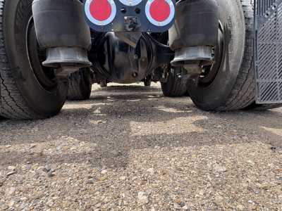 Underside of a Freightliner Cascadia 126 tractor showing rear suspension, driveshaft, and dual rear axles with tires; visible hub assemblies and mud guards.