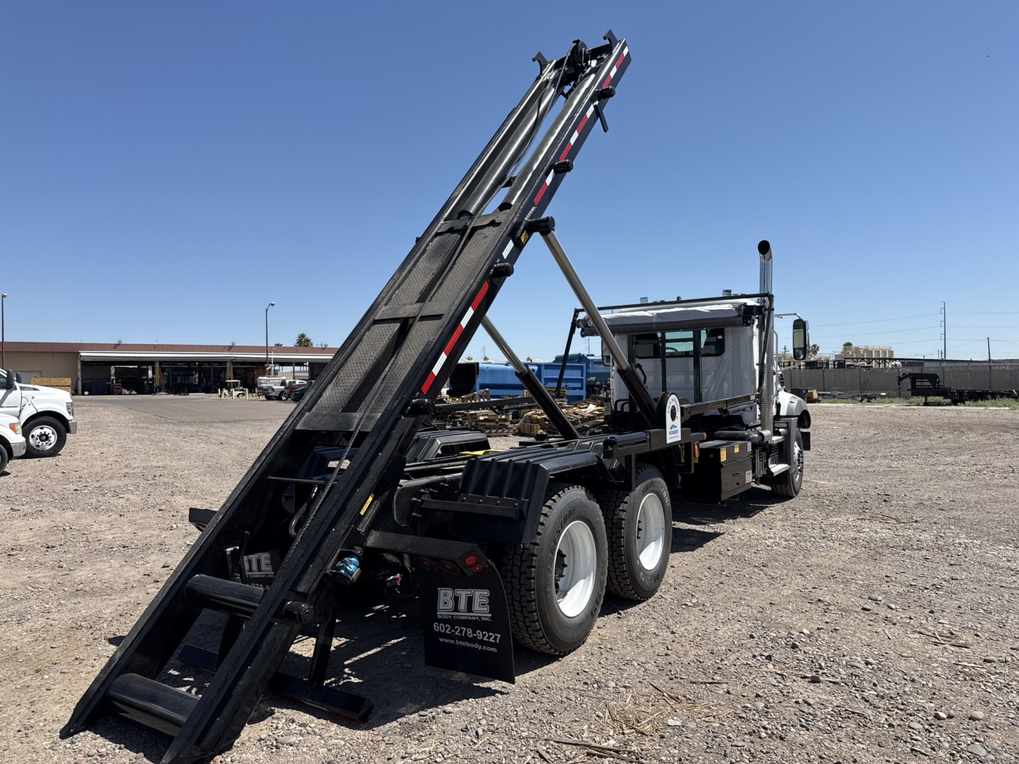 Mack GR64B roll-off truck in a gravel lot showing a tall boom, chassis with six wheels, and cab; no visible text on labels