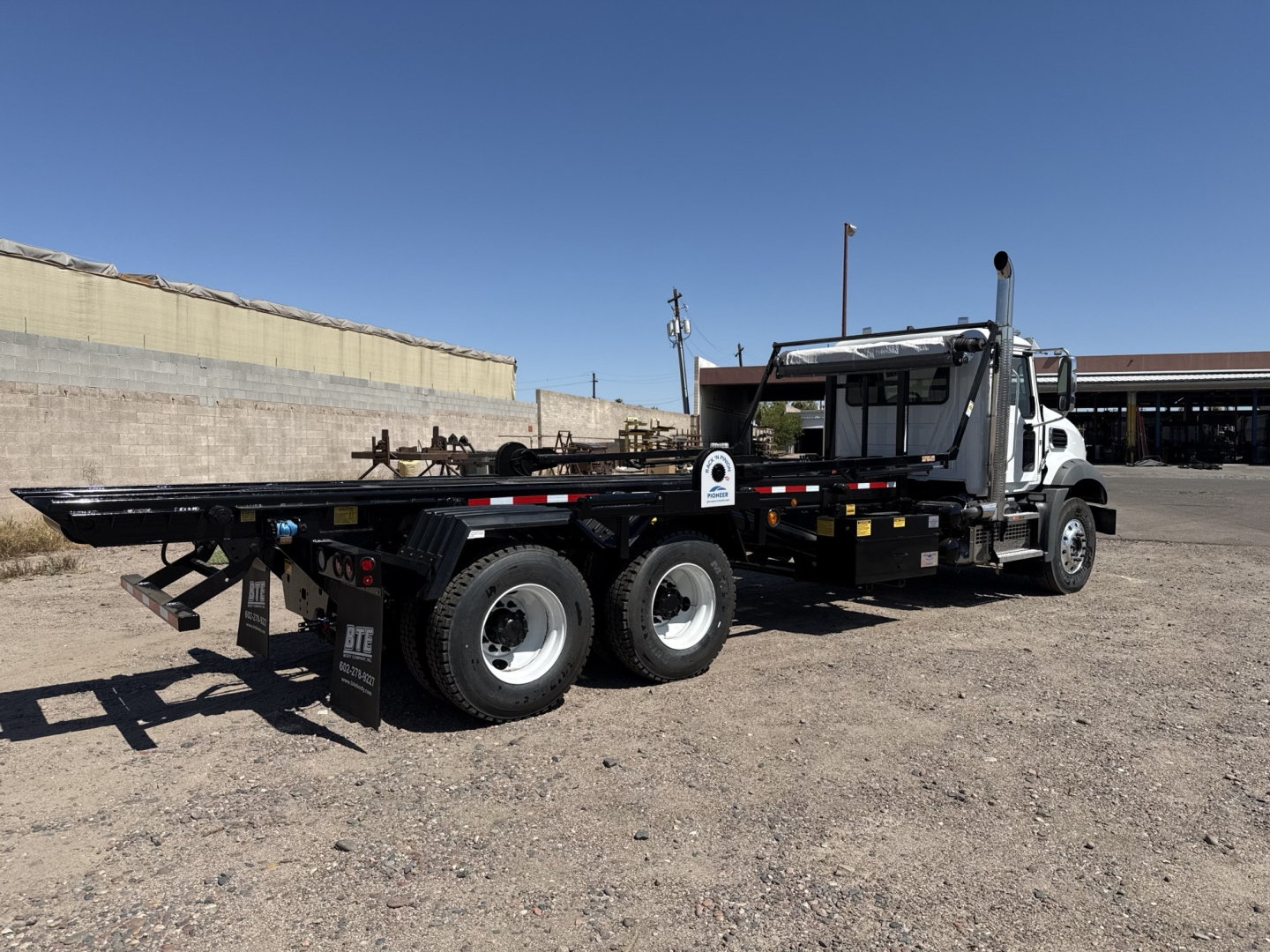 Mack GR64B rolloff truck in a parking lot, side view showing long flatbed and dual rear axles.