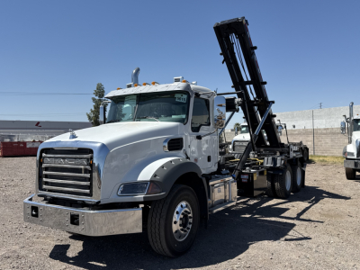 Mack GR64B roll-off truck with a hydraulic arm in a dealership lot.
