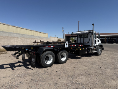 Mack GR64B rolloff truck in a parking lot, side view showing long flatbed and dual rear axles.