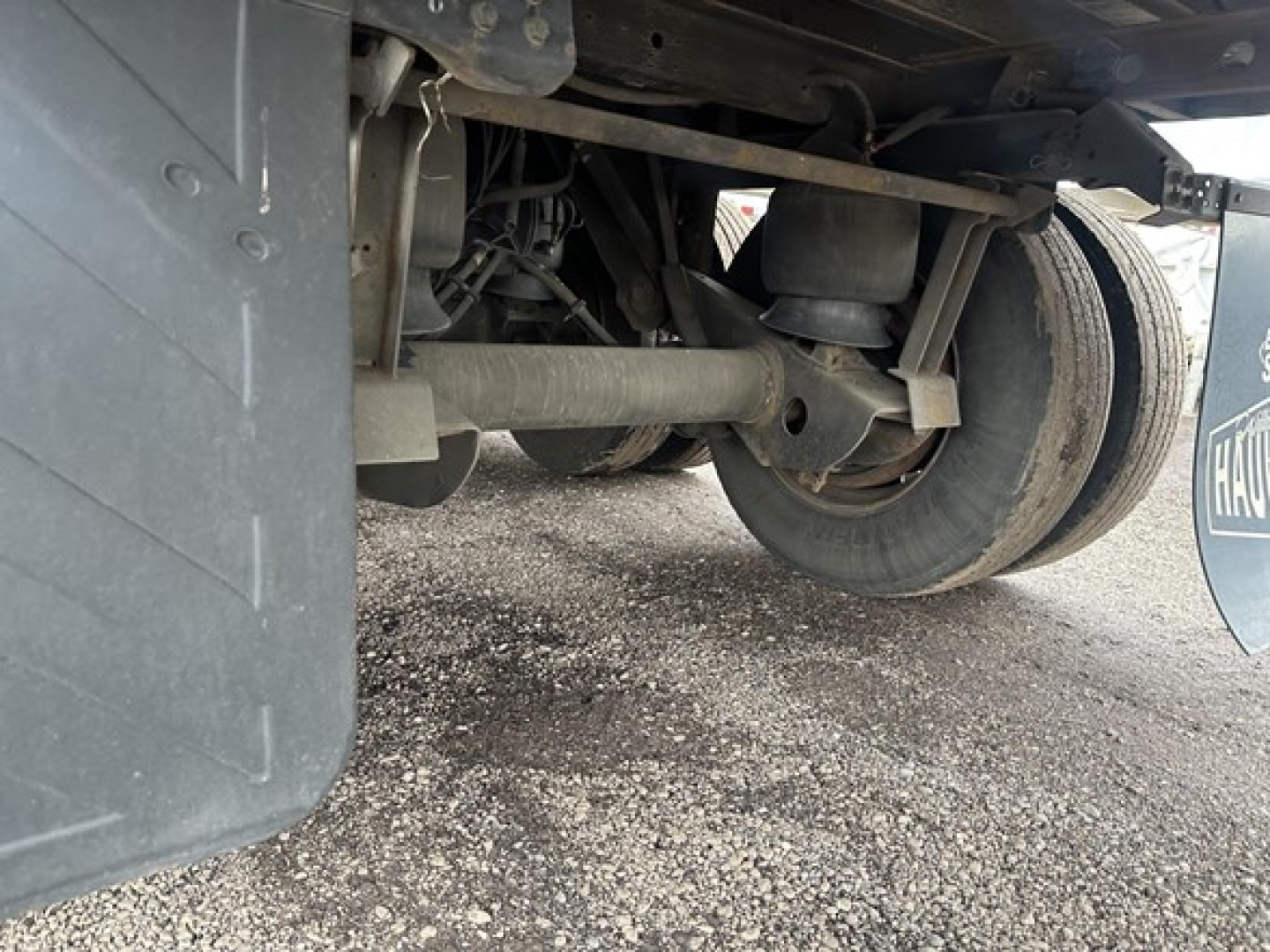 Rear view of a Utility 3000R trailer showing suspension and axle components, including leaf springs and driveline area, with tire and mudflap visible.