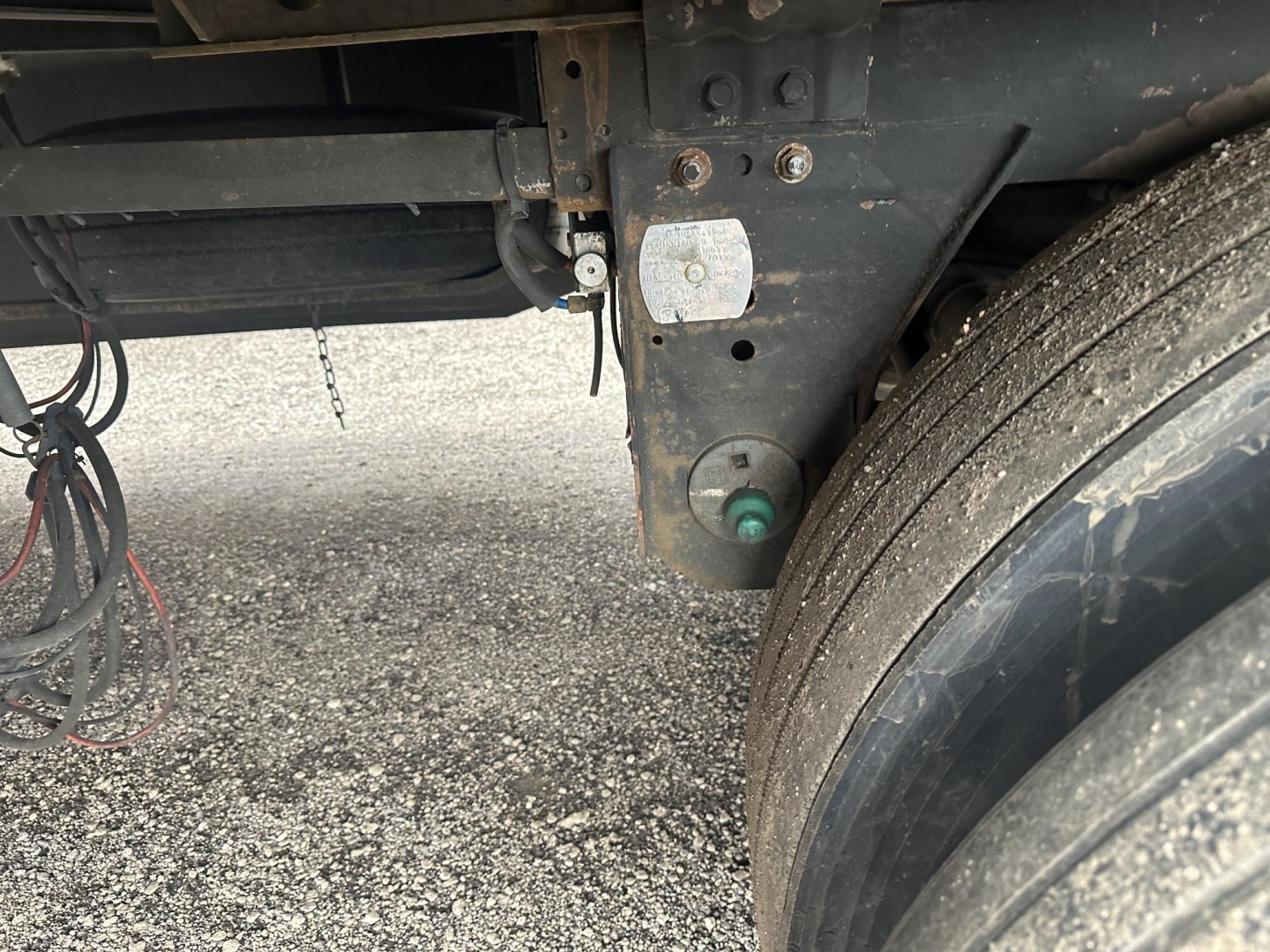 Trailer chassis and dual rear tires showing electrical connector, frame with identification plate, and a green hub area.