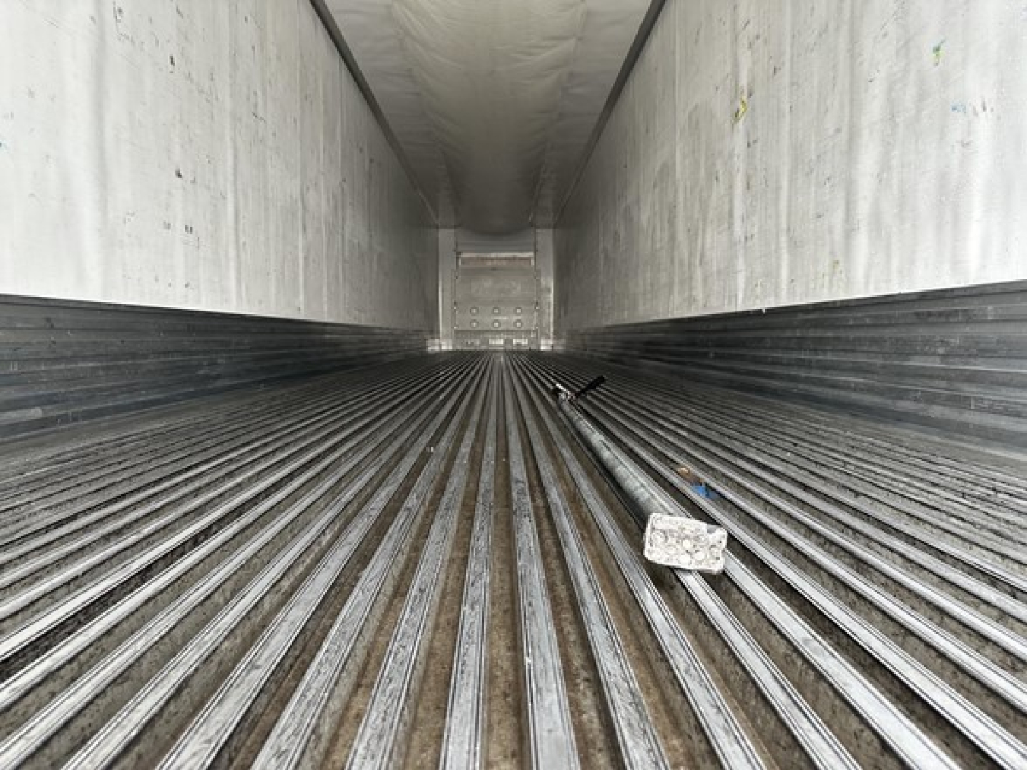 Interior of a Utility 3000R trailer cargo area with ribbed floor and rear door, showing metal walls and a few scattered objects.