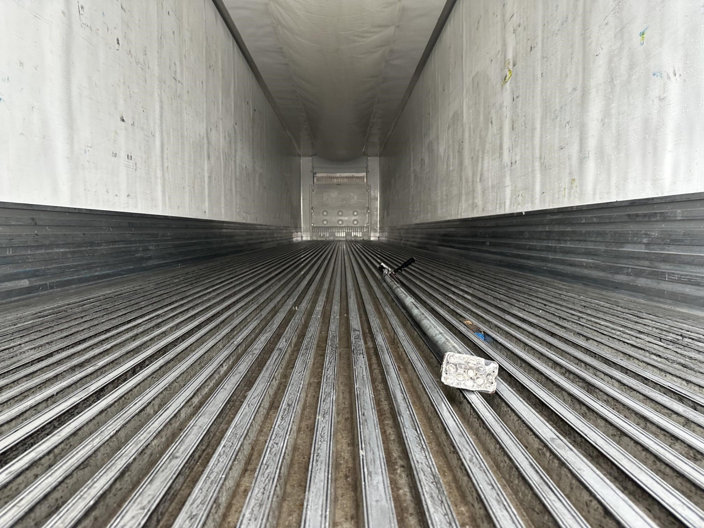 Trailer interior showing ribbed metal floor in a refrigerated trailer with light at far end and a small block on the floor.