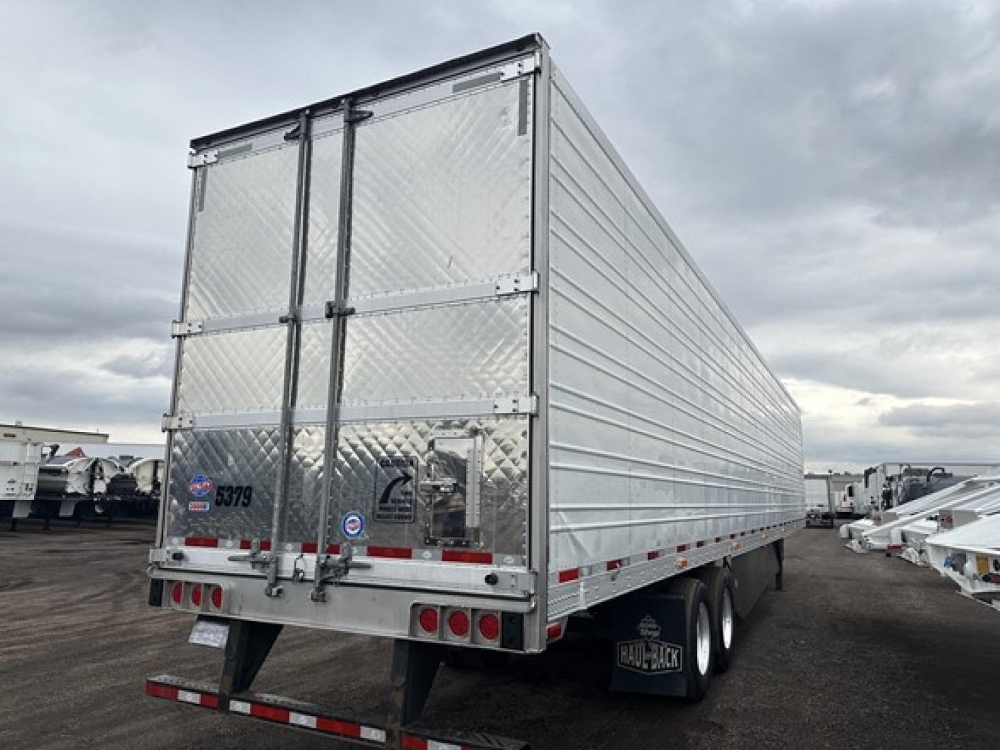 rear of a silver Utility 3000R trailer with doubled doors, diamond plate panels, and trailing undercarriage; rear bumper with lights; various stickers on left door.