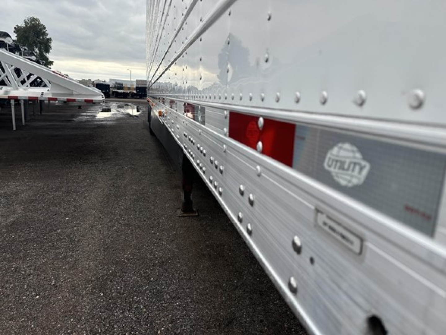 Utility 3000R trailer side panel with riveted aluminum exterior and Utility logo, reflection in metal, viewing along the bottom edge.