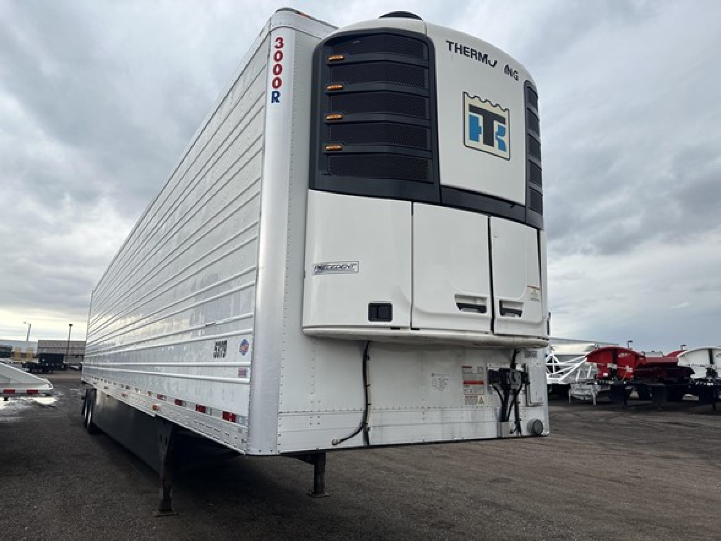 Utility 3000R trailer with Thermo King refrigeration unit at front, white body, vertical '3000R' text on nose, chassis landing legs visible in foreground, other trailers in background.