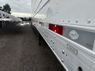 Trailer side panel showing Utility brand logo and riveted aluminum walls of a 2023 Utility 3000R trailer in a lot.