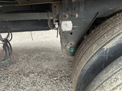 Trailer showings undercarriage with wheels and hydraulic components; visible labels and wiring near rear of chassis.