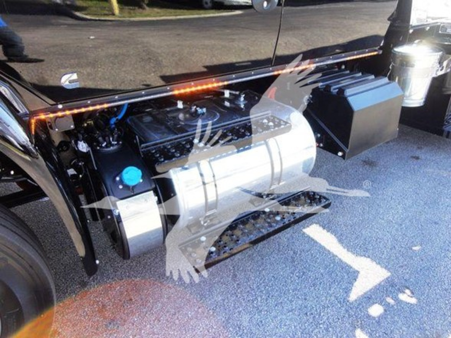 Truck engine bay with large aluminum fuel tank, blue coolant cap, and black toolbox on side; MV International truck components visible.