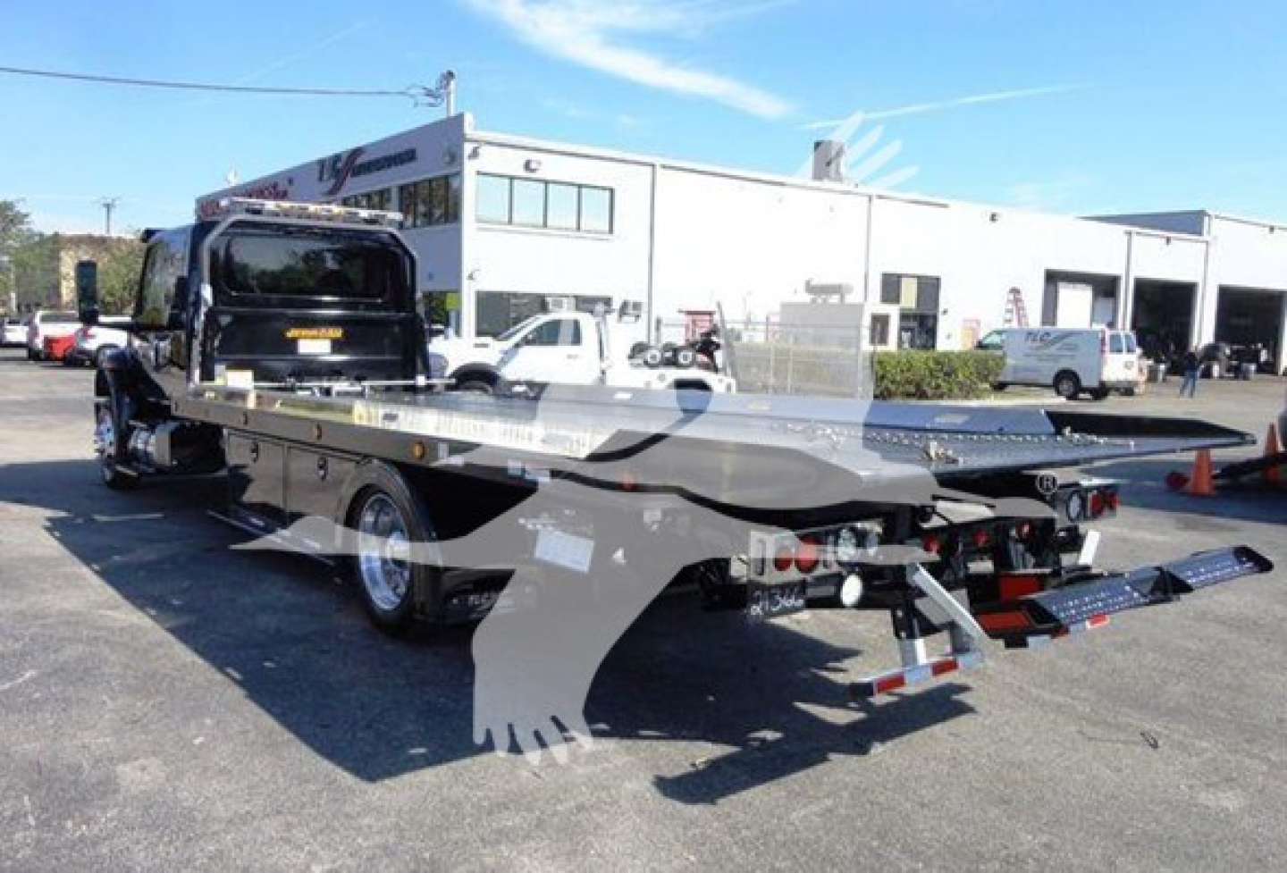 Truck bed rollback tow truck showing flatbed with rear D-rings and warning lights.