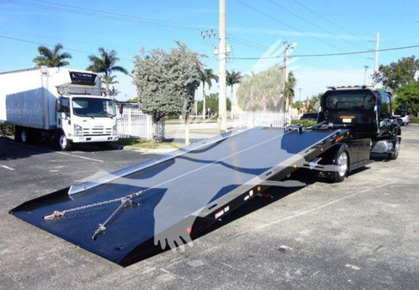 1992-2022 International MV rollback truck with a long flatbed ramp in view and hitch, showing a white cab and black trailer surface.