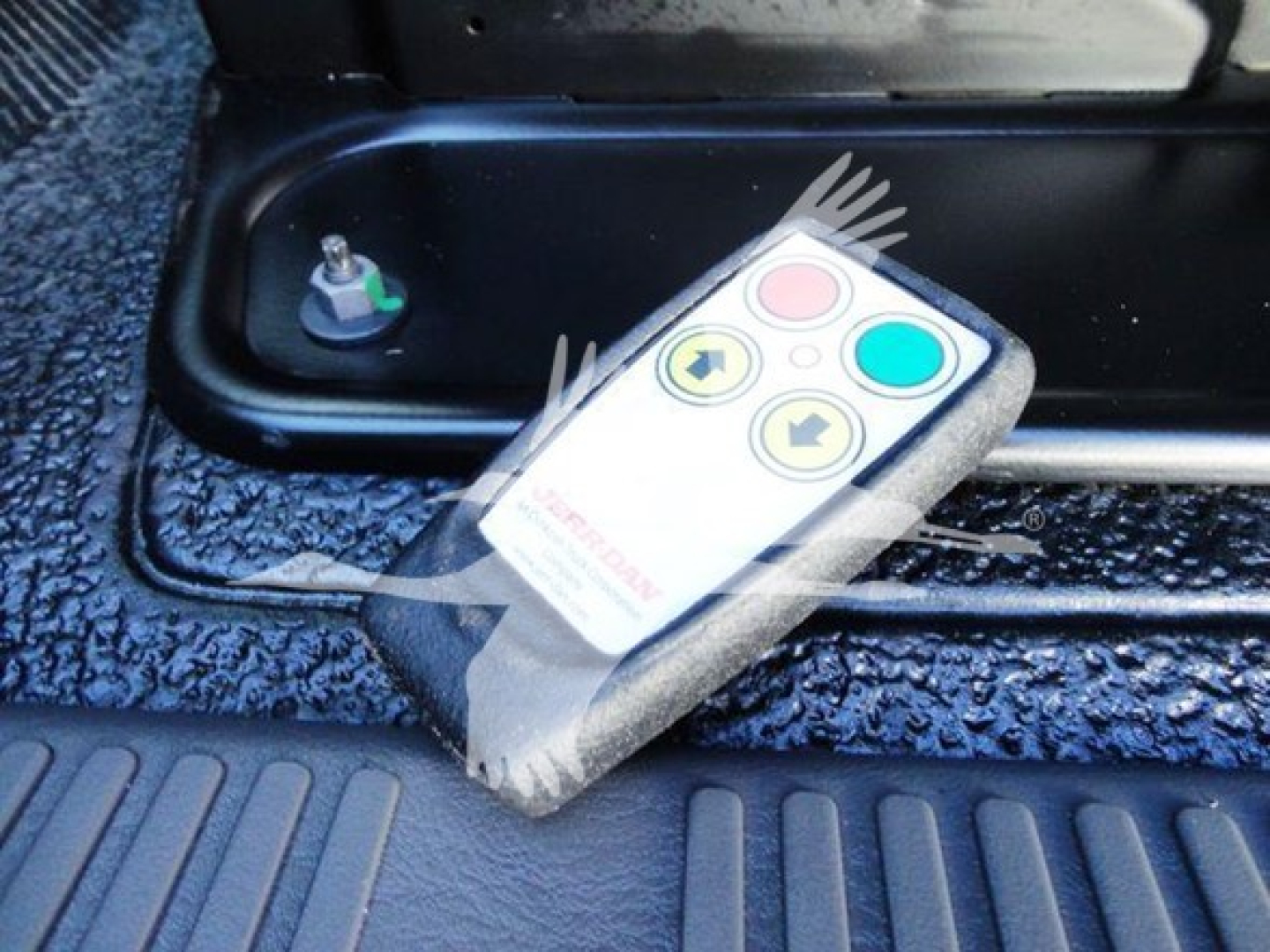 Remote control device with colored buttons resting on a textured surface near a blue hydraulic console in a truck.