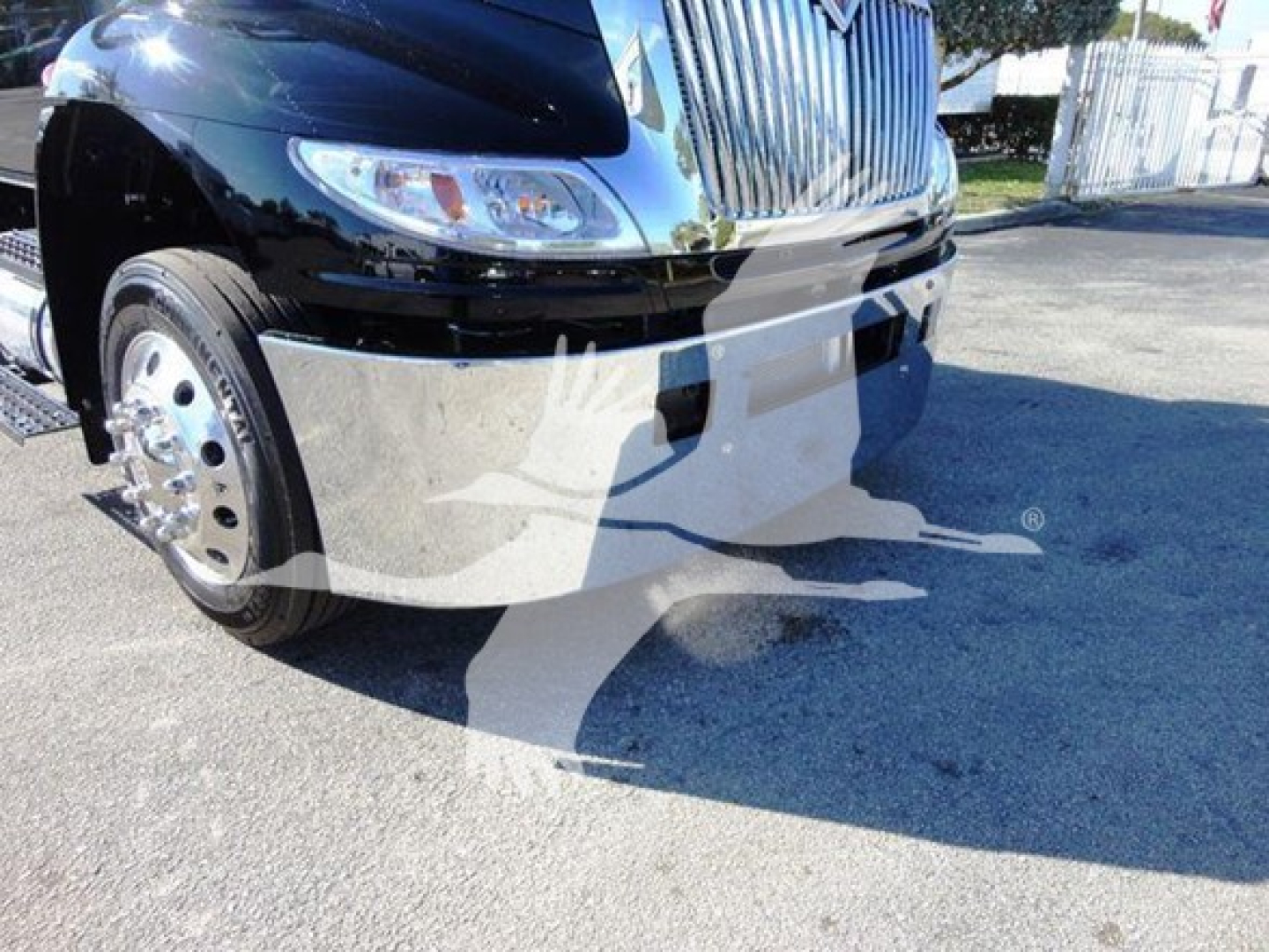 Truck front end and front left wheel of a 2022 International MV rollback truck showing chrome grille, headlight, and bumper.