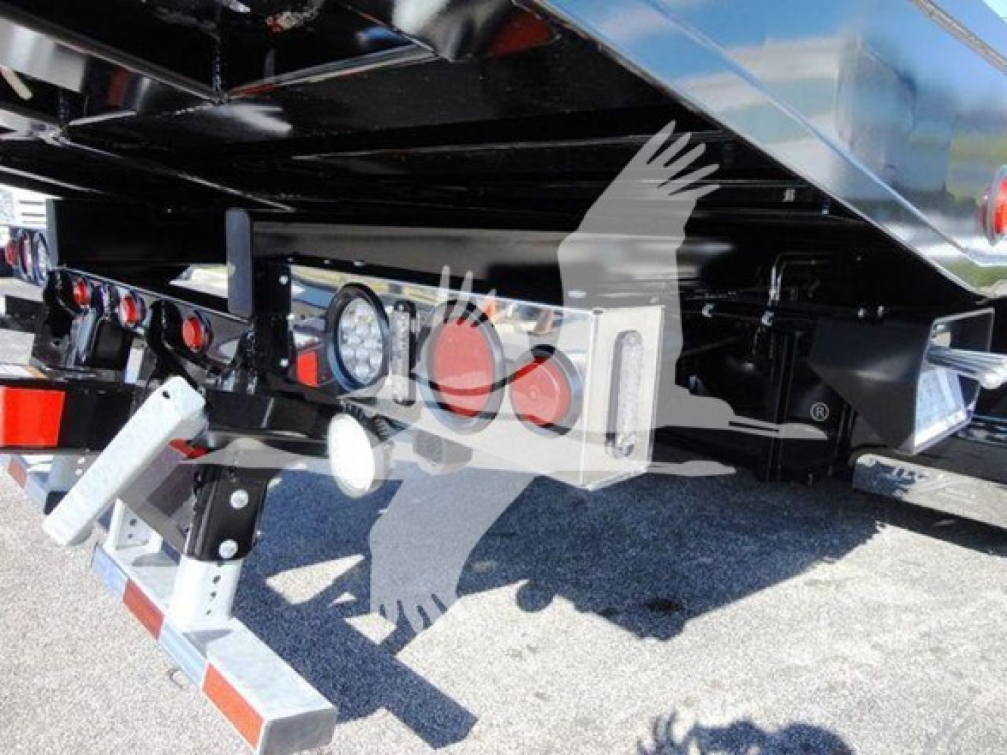 Truck undercarriage showing rear bumper, hitch, and license-plate mount with lights and hydraulic components.