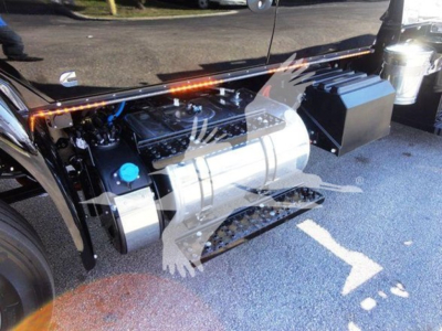 Truck engine bay with large aluminum fuel tank, blue coolant cap, and black toolbox on side; MV International truck components visible.