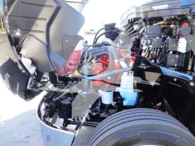 Truck engine bay showing International MV engine components, hoses, battery, and wiring harness with visible coolant reservoir and various labels.