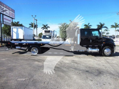 Flatbed tow truck side view showing International MV chassis with long lowbed parked in lot.