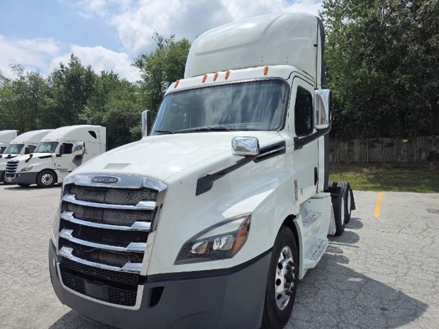 Truck cab exterior showing Freightliner Cascadia sleeper with white paint and chrome grille, front view in parking lot.