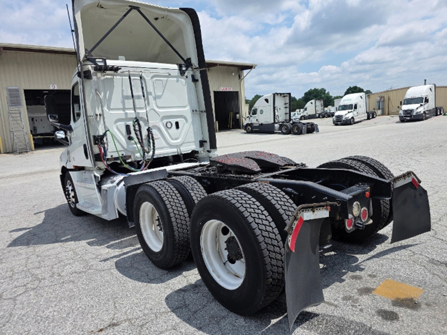Truck cab rearview showing fifth-wheel and dual rear axles with mud flaps and exposed engine bay, Freightliner Cascadia 126 style chassis.