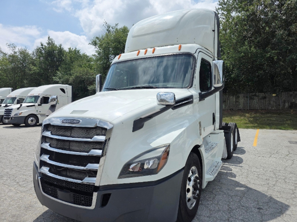 Truck cab exterior showing Freightliner Cascadia sleeper with white paint and chrome grille, front view in parking lot.