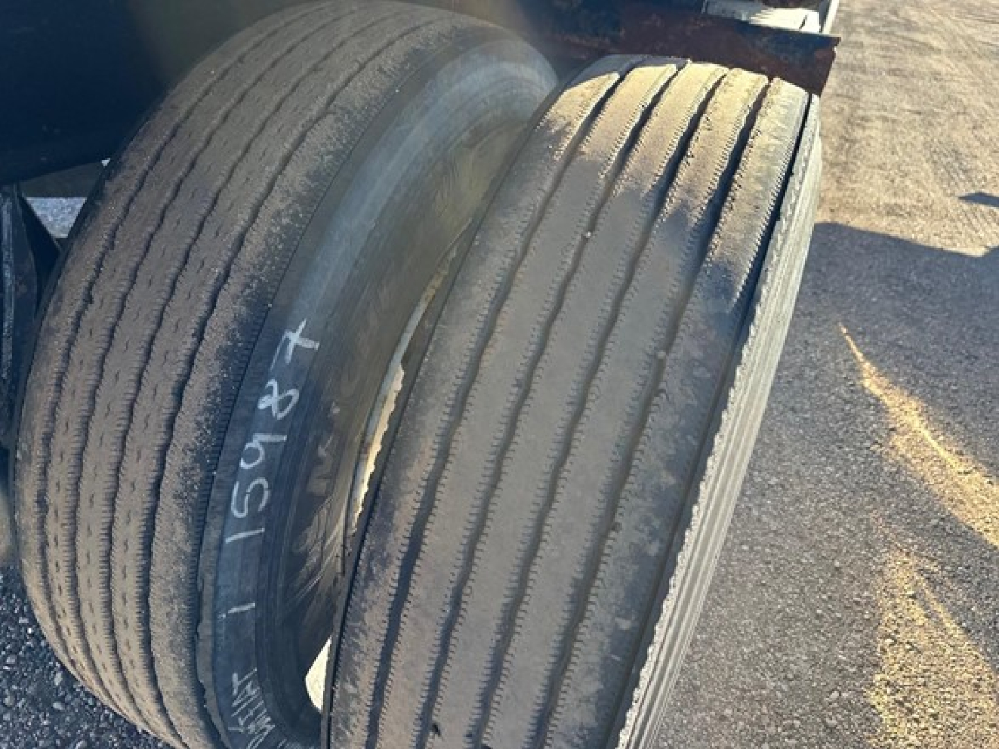 Flatbed trailer tires mounted on wheel hubs; tread visible with parallel grooves; faint white chalk markings on left tire.