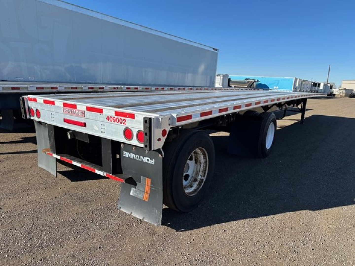 Flatbed trailer showing rear and side, Fontaine logo, dual rear tires, reflective striping, and wheel mudflap.