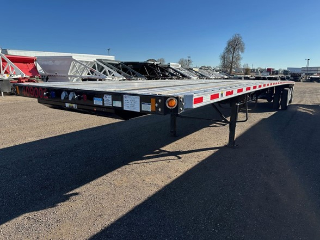 Flatbed trailer showing metal deck and safety rails with reflective tape along sides and dual rear axles.