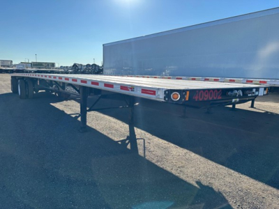 Flatbed trailer showing side rails with reflective tape and rear lights; visible text includes '409002' in pink on the rear frame.