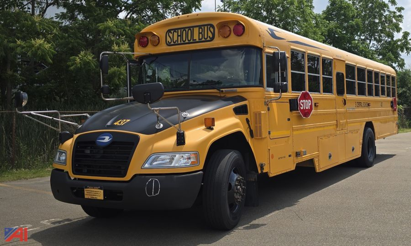 School bus front-left view showing 'SCHOOL BUS' sign on roof and stop sign extended at side.