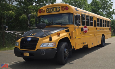School bus front-left view showing 'SCHOOL BUS' sign on roof and stop sign extended at side.