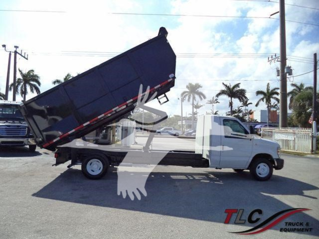 Ford E450 dump truck in-service showing dumping bed raised with hydraulic cylinder and white cab, VIN 1FDXE4FS3BDA96309.