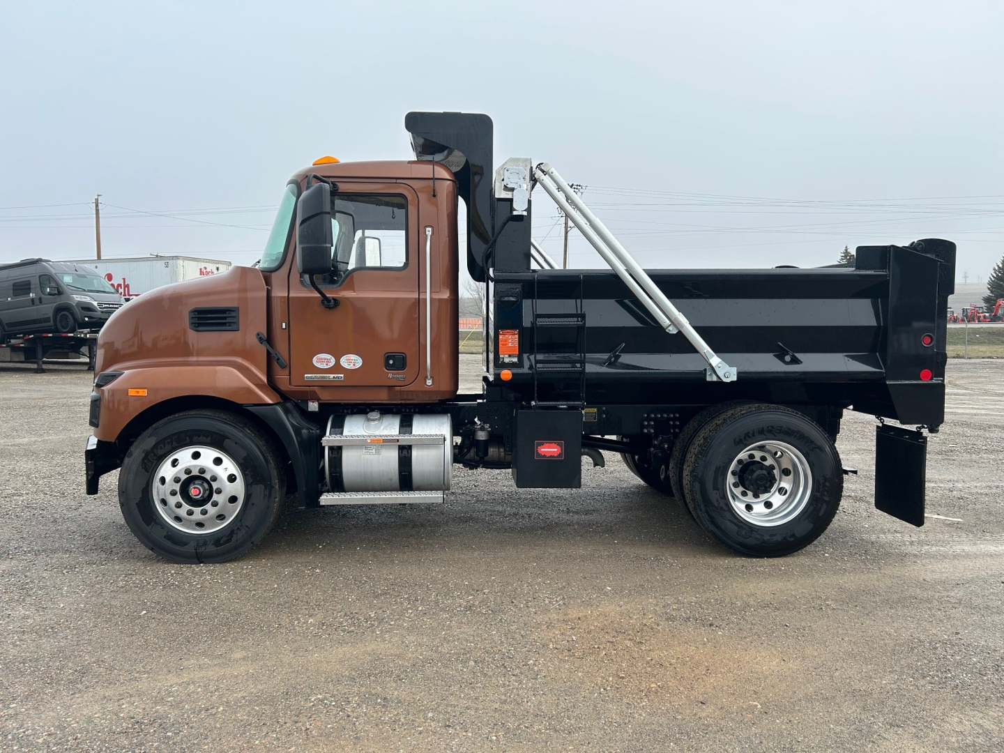 Dump truck side view showing Mack MD7 cab in brown with black dump bed and hydraulic hoist.