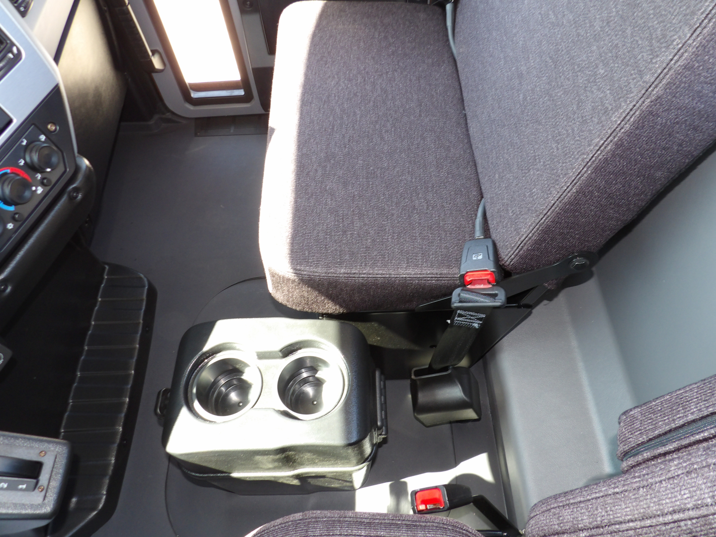 Truck cab interior showing driver seat and center console with two cup holders and seat belt buckles in a Mack MD7 cab.