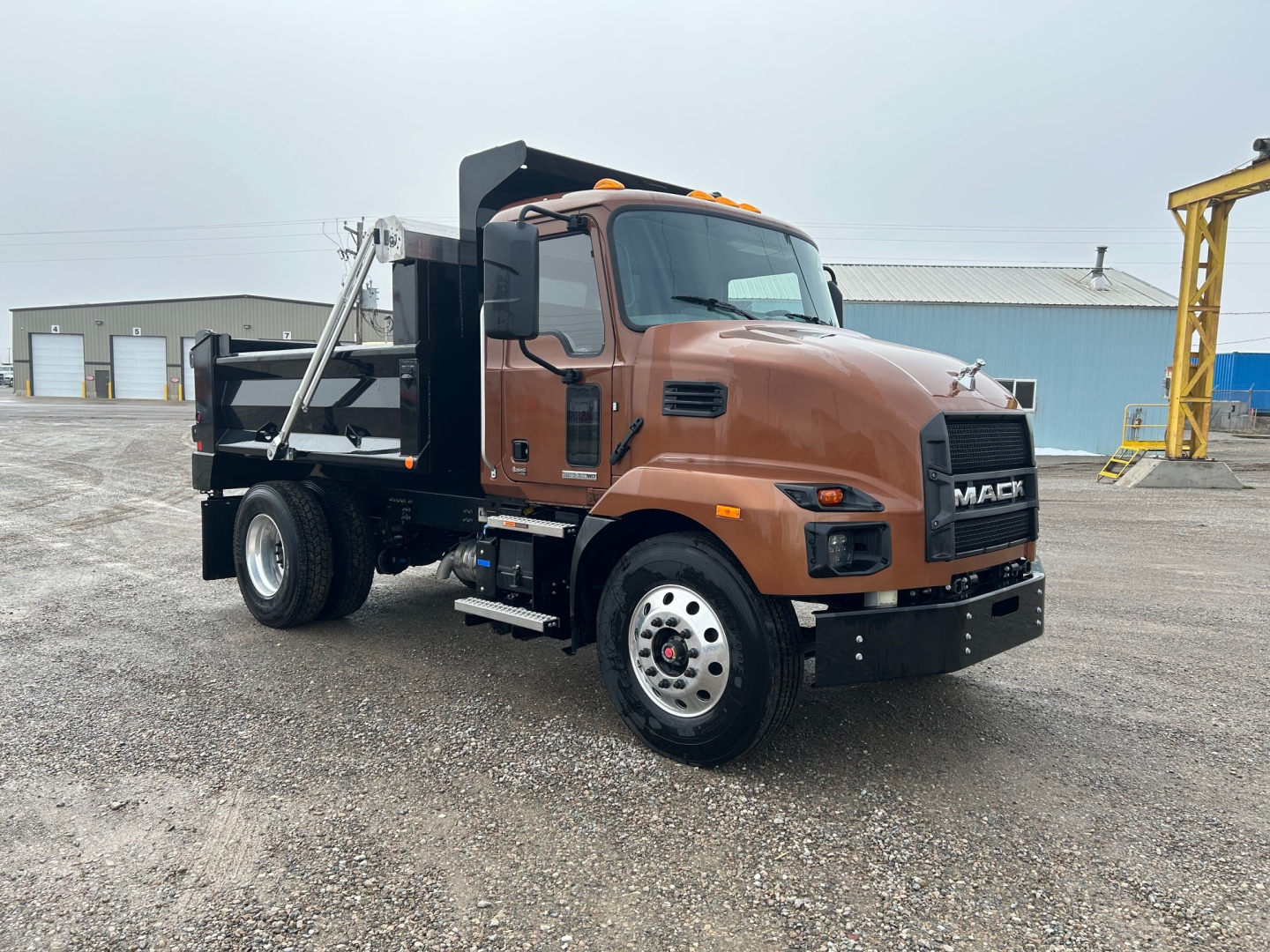 Mack MD7 dump truck showing brown cab and black dump bed with chrome wheels.