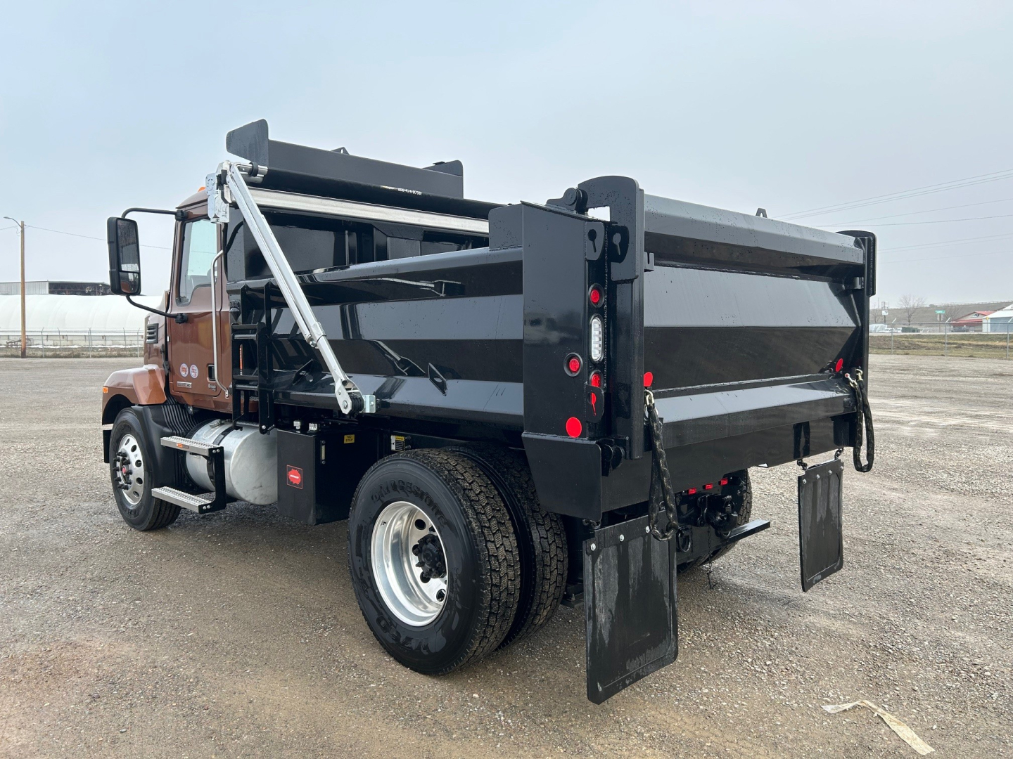 Dump truck bed with black steel dump body and rear gates, MD7 category, new Mack MD7 truck, side view showing dual rear wheels and hydraulic dump mechanism