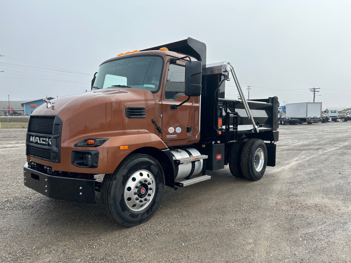Dump truck front three-quarter view showing Mack MD7 cab and steel dump bed with black grille and headlights.