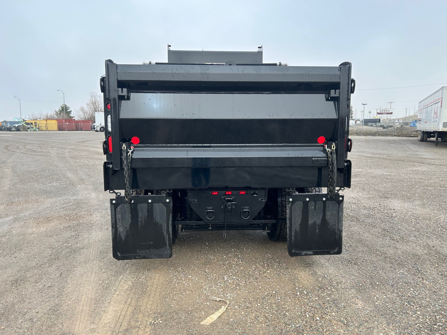 Dump truck rear view showing dump bed, tailgate, and dual rear tires in a gravel lot.