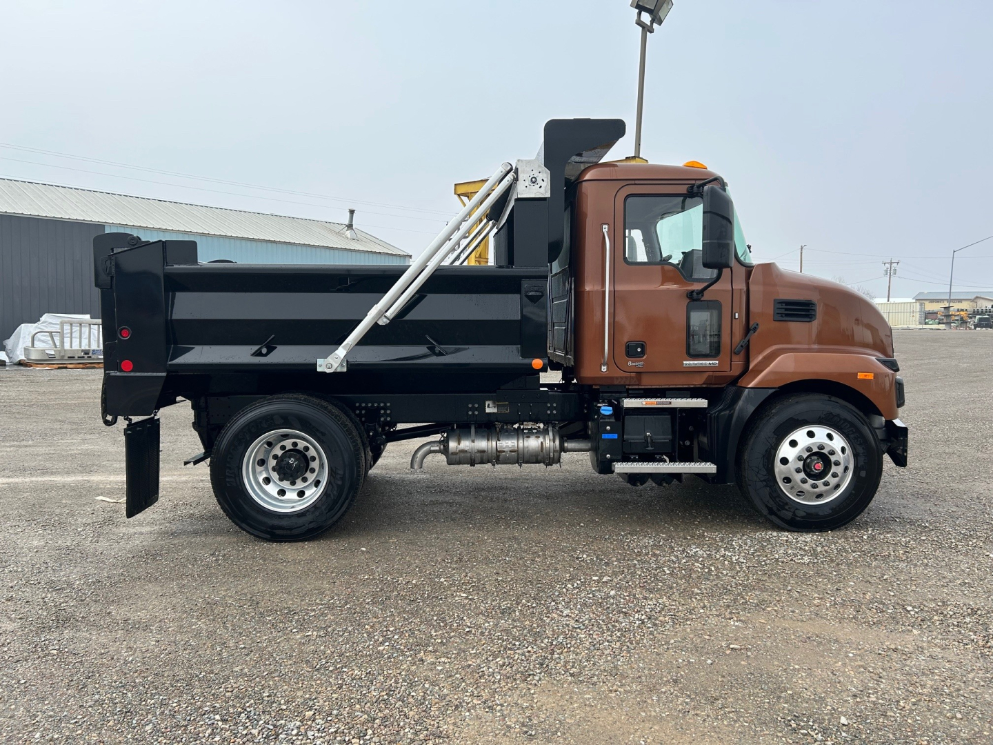 Side view of a brown and black Mack MD7 dump truck with a black dump bed, chrome exhaust, and silver wheels. VIN plate and stock number not visible in image.